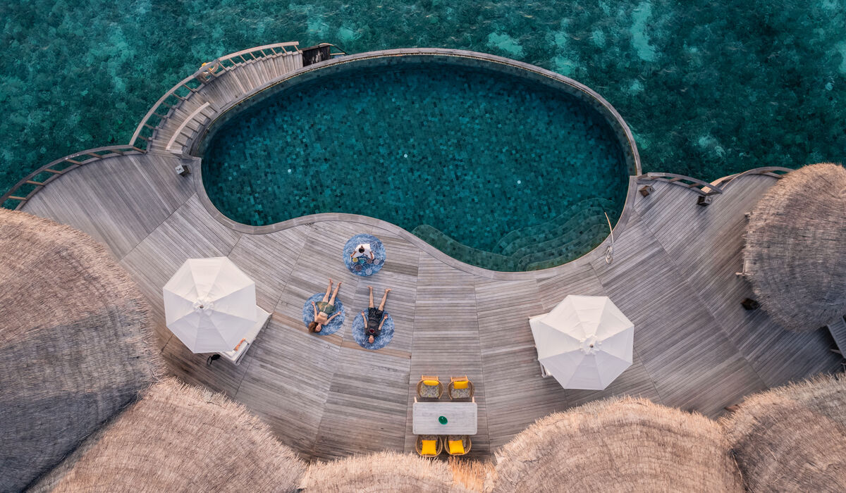 Aerial image of two people and a yoga instructor practicing yoga on a deck of an over water villa with private pool at The Nautilus Maldives